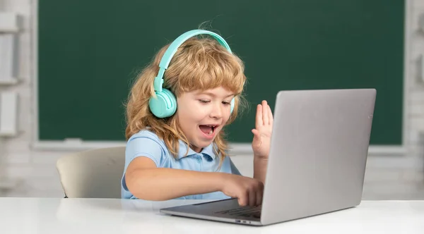 Mały chłopiec w słuchawkach ogląda lekcje wideo na komputerze w szkole, dziecko w słuchawkach ma lekcje online, za pomocą laptopa. Badania zdalne i edukacja. — Zdjęcie stockowe