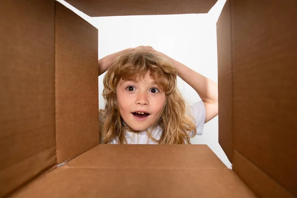Divertente sorpresa scioccato bambino ragazzo sta aprendo regalo e guardando dentro scatola di cartone. Pacchetto apertura bambino. — Foto Stock