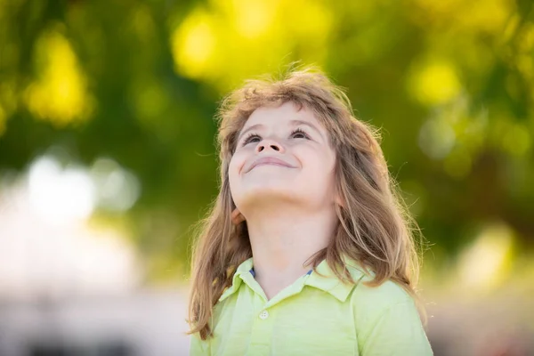 Niño feliz mirando hacia arriba, adorable niño encantador. Retrato alegre de niño pequeño sobre fondo verde de la naturaleza afuera. — Foto de Stock