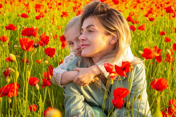 Madre e hija abrazándose en el prado de primavera. Hermosa niña con madre joven están usando ropa casual en el campo de las flores de amapola. Familia en campo de amapola de primavera. —  Fotos de Stock