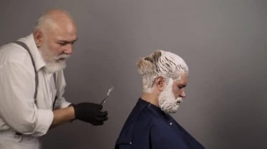 Gri renk sürecinde saç boyası. Kuaför, erkek modellerin saçlarına renkli renkler sürüyor. Reklamcılık ve berber dükkanı konsepti. Stüdyoda saç kurutan profesyonel kuaför..