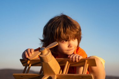 Tahta oyuncak uçakla oynayan çocuk pilot olma hayali kuruyor. Çocuk rüyaları. Ahşap uçaklı çocuk pilot. Tatlı çocuk suratı..