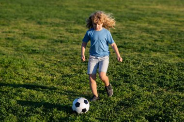 Futbolcu. Çocuklar yaz stadyum sahasında futbol oynarlar. Küçük çocuk topa vuruyor. Küçük çocuk kaleye ateş ediyor, çocuk futbol topunu tekmeliyor.