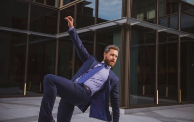 Heyecanlı iş adamı kollarını kaldırıyor ve dışarıda ofis binası ile durarak pozitifliğini gösteriyor. Dans eden iş adamı. Zirvede kalmak.