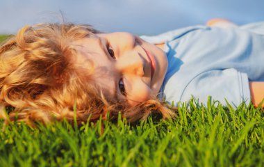 Yeşil çimlerin üzerinde uzanmış hayal kuran gülümseyen küçük bir çocuğun portresi. Doğanın tadını çıkaran sevimli bir çocuk. Sağlıklı kaygısız çocuk yaz parkında çimlerin üzerinde oynuyor..