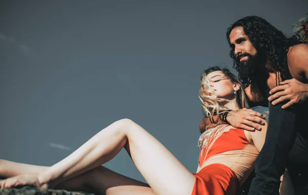 사랑하는 커플. 건강 한 턱수염을 가진 남자가 맑은 여름날푸른 하늘 배경의 우아 한 빨간 드레스를 입은 젊은 섹시 한 여자를 안고 있습니다. 강한 관계 와사 랑을 누리고 있는 부부. — 스톡 사진