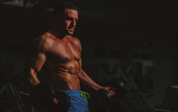 Silny mężczyzna z hantlami na siłowni. Bodybuilder szkolenia biceps przez ćwiczenia treningowe. Sportowiec ze sportowym ciałem. — Zdjęcie stockowe