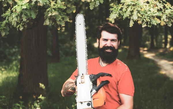 Stylish young man posing like lumberjack. Lumberjack worker standing in the forest with chainsaw. Deforestation.