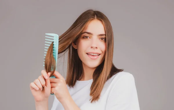Woman is making hairstyle with comb. Beautiful young woman holding healthy and shiny hair, studio. — Stock Photo, Image