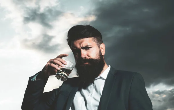 Portret van een knappe bebaarde zakenman in elegant pak die een whisky drinkt. — Stockfoto