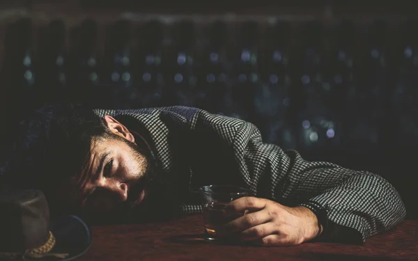 Расстроенный бородатый мужчина, пьющий алкоголь, сидит за барной стойкой со стеклом и пьет виски в одиночестве. Грустный депрессивный пьяный парень, имеющий проблемы с алкоголизмом, алкоголизмом. — стоковое фото