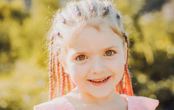 Menina sorrindo com dreadlocks penteado. Criança com cabelo elegante ao ar livre. Criança feliz lá fora. — Fotografia de Stock