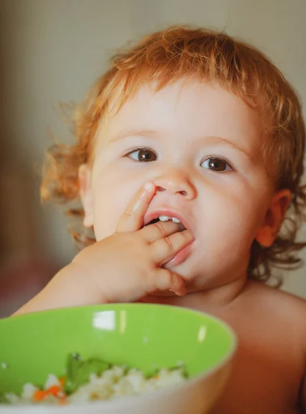 Divertido bebé en la cocina comiendo con los dedos del plato. — Foto de Stock