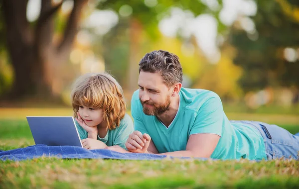 Ευτυχισμένος πατέρας χρησιμοποιώντας φορητό υπολογιστή χαλαρώστε με το γιο μαθητή κρατώντας φορητό υπολογιστή διασκεδάστε μαζί, χαμογελαστός μπαμπάς και το μικρό παιδί αγόρι απολαύσετε το Σαββατοκύριακο με gadgets έξω στη φύση. — Φωτογραφία Αρχείου