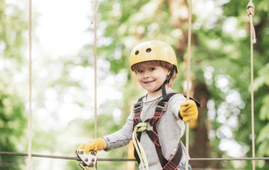 Mutlu çocuk çocuk yüksek ağaç ve halatlar tırmanırken arıyor. Ağaçların arasında bir ip parkta güzel bir çocuk portresi. Küçük çocuk çocukluk yıllarını zevk.