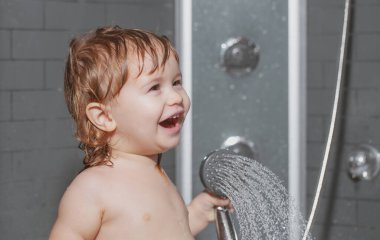 Duşun altında yıkanan çocuk. Küçük bebek saçını banyoda yıkıyor..