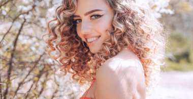 Kıvırcık saçlı çiçek arka plan üzerinde. Güzel bahar kadın sonbaharda doğa arka plan. Neşeli kaygısız kadın Park güneşli bahar gününde. Kozmetik güzellik kavramı.