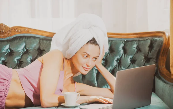 Attraente studentessa in pigiama e asciugamani che studiano a casa, usando il computer portatile, bevendo caffè. — Foto Stock