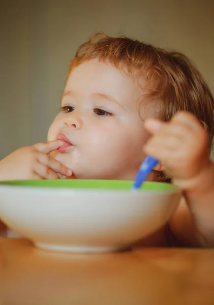 Grappig klein baby in de keuken eten met vingers van plaat. Lik smakelijke vingers. — Stockfoto