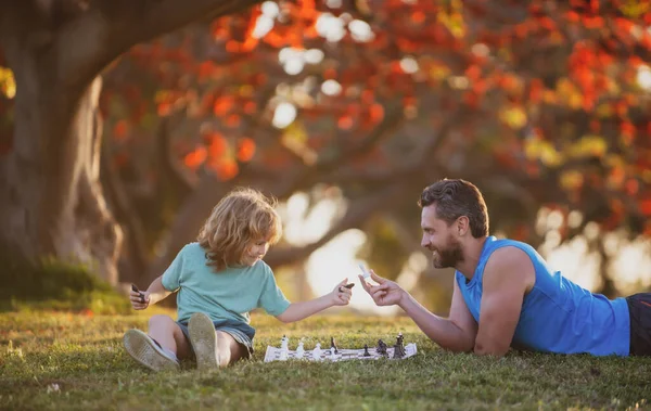 Bambino figlio sdraiato sull'erba e giocare a scacchi con il padre. — Foto Stock