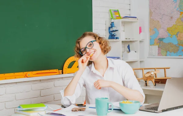 Vrouwelijke leraar aan haar bureau markeert leerlingen werken. Mooie leraar die lacht naar de camera op school. Universiteitsstudent. — Stockfoto