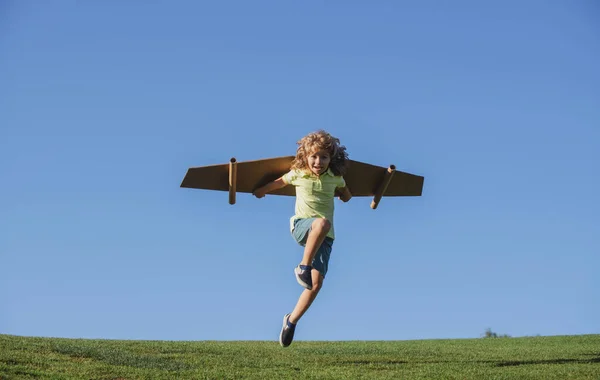 El niño juega al astronauta piloto. Niño soñando con convertirse en un aviador astronómico. Niño sobre un fondo azul del cielo jugando con un plano de alas de cartón. — Foto de Stock