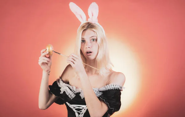 Hermosa rubia sensual. Mujer joven y feliz pintando huevos sobre un fondo rojo. Una joven atractiva con orejas de conejo. Conejo de conejo. Cara de expresión . — Foto de Stock