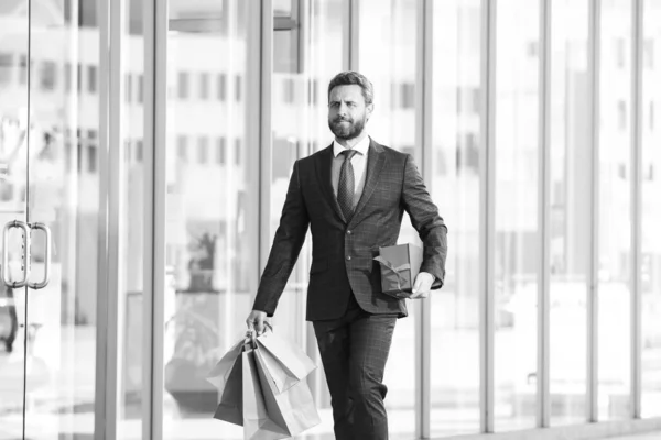 Un uomo ricco. Un uomo d'affari che fa shopping in un centro commerciale. Buon uomo d'affari in giacca e cravatta. Uomo shopaholic a piedi sulla strada commerciale con un sacco di borse della spesa. — Foto Stock