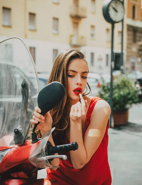 A aplicar maquilhagem na rua. Menina de moda sexy com lábios vermelhos colocar batom olhando em um espelho de moto. — Fotografia de Stock