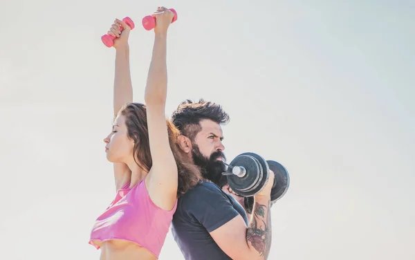 Fit sexy couple on sky background with dumbbells. Fitness concept. Sports couple training with dumbbell. Healthy coupl life style. Sporty woman in sexy pink sportswear. — 图库照片