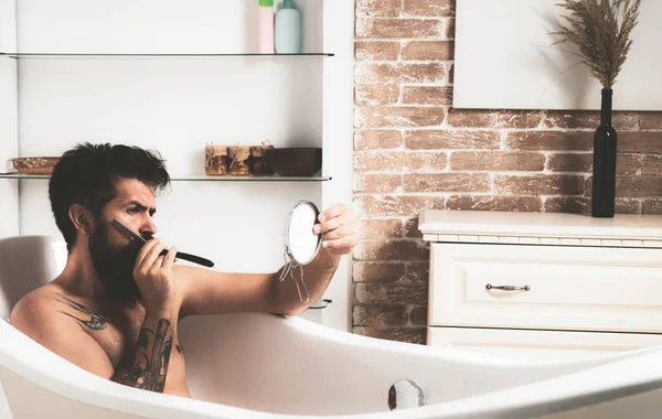 ハンサムな髭を生やした男が風呂に入っている。髭を生やしてる。鏡を手に髭を生やした髭の男。朝の衛生. — ストック写真