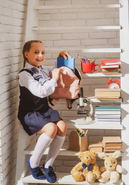 School meisje bereidt rugzak voor op school. Onderwijs voor kinderen. Terug naar school. Een schoolmeisje die boeken verzamelt in een schooltas. Jong schoolmeisje gaat om kennis te krijgen. — Stockfoto