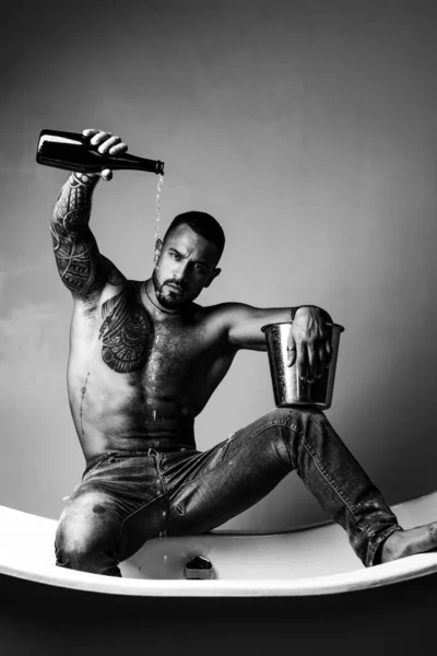 Champagne o festa del vino. Concetto festival del vino. Un bell'uomo con un corpo tatuato. Un bell'uomo brutale su sfondo grigio. Mude modello maschile con corpo nudo. — Foto Stock