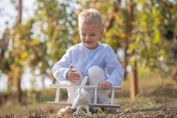 Los niños se divierten con el avión de juguete en el campo contra el fondo de la naturaleza. Aventura y vacaciones concepto de los niños. Verano en el campo. Sueños de viajes. Niño soñando con un avión de juguete. — Foto de Stock