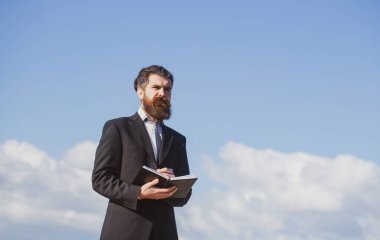 Kendine güveni tam bir iş adamı, elinde not defteri ve kalemle gökyüzü arka planında.