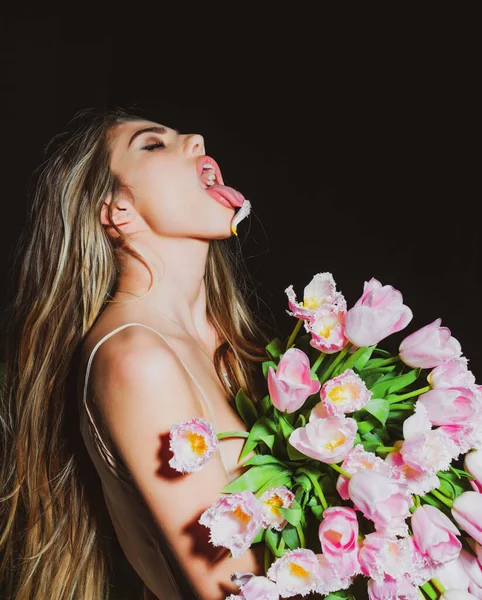 Smyslná dívka s květinovou kyticí izolovanou na černé. Mladá krásná žena drží kytici růžových tulipánů nad izolovaným pozadím vyčnívající jazyk, legrační výraz. Emoční koncept. — Stock fotografie