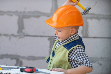 İnşaatta tadilat için aletleri olan küçük miğferli bir mimarın portresi. İnşaatçı çocuk, marangoz çocuk ve inşaatçı aletleri var. Çocuk tamircisi ve tamircisi..