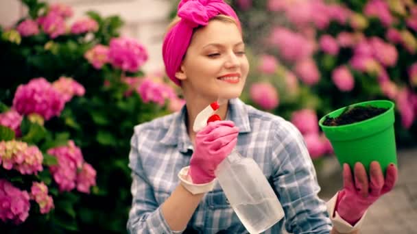 Mujer regando flores en maceta. Jardinería ib patio trasero. Mujer rubia alegre plantando flores en el jardín. — Vídeo de stock