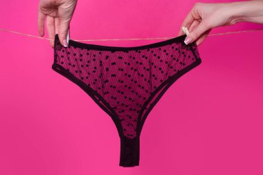 Kadınların elleri ipte asılı erotik siyah iç çamaşırları, mor arka planda izole. Dantelli iç çamaşırı, kadın iç çamaşırı..