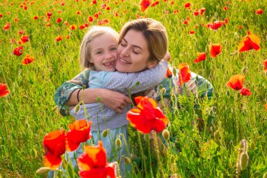 Anne ve kızı gelincik çayırında sarılıyorlar. Anne ve kız gelincik çiçekleriyle tarlada dinleniyorlar. Kadın ve kız eğleniyor ve özgürlüğün tadını çıkarıyor..