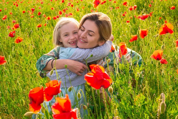 Μητέρα και κόρη αγκαλιάζονται σε ένα λιβάδι με παπαρούνες. Η μαμά και η μικρή ξεκουράζονται στο χωράφι με τα λουλούδια. Η γυναίκα και το κορίτσι διασκεδάζουν και απολαμβάνουν την ελευθερία. — Φωτογραφία Αρχείου