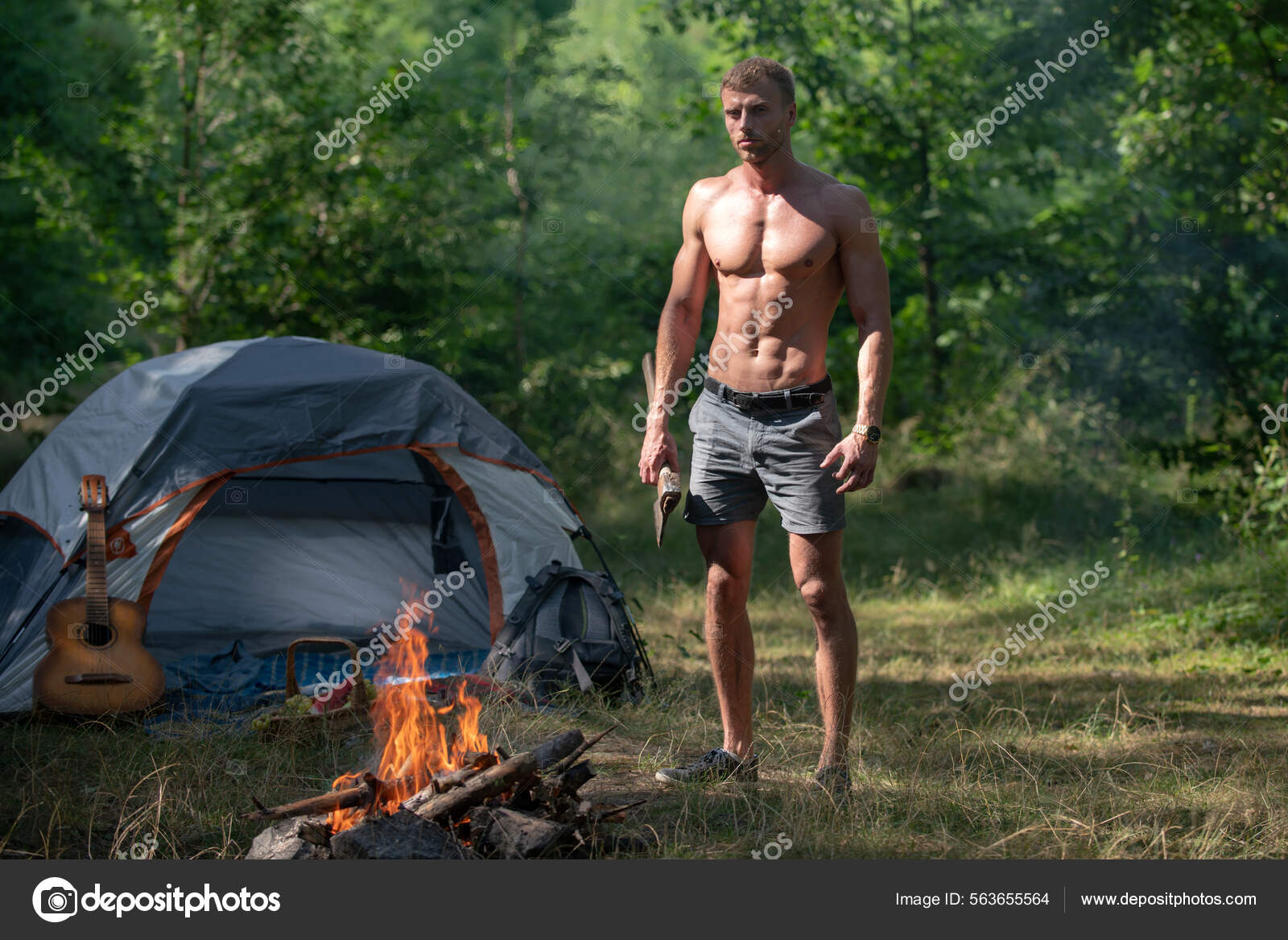 Camping season with campfire. Man with naked torso, picnic tourism camp.  Man lumberjack with axe look at bonfire flame on summer day on natural  landscape. Traveling, camping hiking vacation. Stock Photo by ©