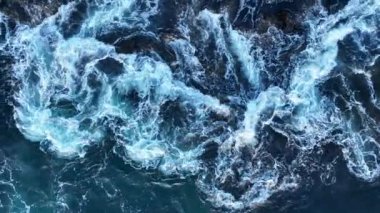 Dalga sahili, okyanus dalgaları kayaların üzerinden geçiyor. Dalgalarda köpükle su sıçrıyor.