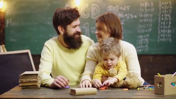 Garçon de l'école primaire. Joyeux livre de dessin familial. Mère père et fils lisant les devoirs sur le livre. Les parents sont fiers des progrès de l'enfant fils. — Video