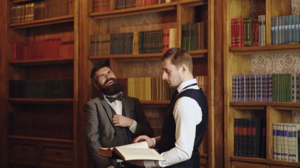 Företagsanställda chattar i biblioteket. Vetenskapsmän pratar. Professor och student diskuterar i biblioteket. Man läser bok i klassiskt biblioteksskåp. Hembiblioteket. — Stockvideo