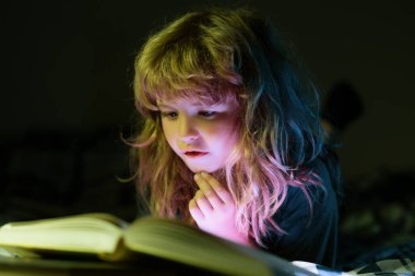 Çocuk uyumadan önce yatakta kitap okuyor. Evdeki küçük çocuk yatakta uzanıp kitap okuyor. Eğitim ve okuma kavramı.