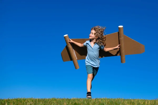 小さな子供は宇宙飛行士やパイロットを演じる。青い空を背景に走っている子供。紙の翼ジェットパックの夢を持つ子供たち。子供たちは飛ぶ夢を想像する。おもちゃのジェットパックと面白い子供. — ストック写真