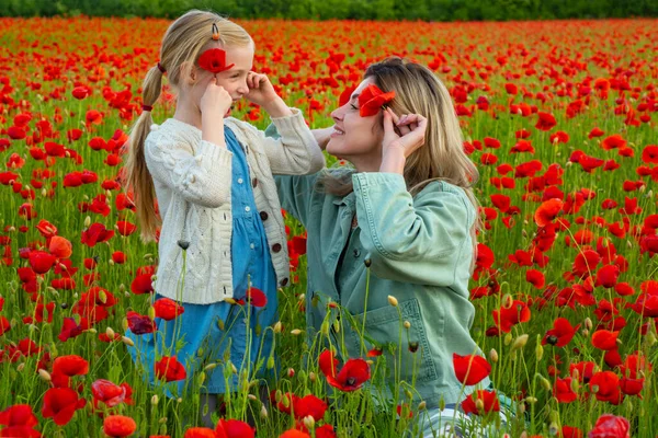 Hermosa niña con madre joven están usando ropa casual en el campo de las flores de amapola. Familia en el campo de amapola de primavera. Feliz maternidad.. —  Fotos de Stock