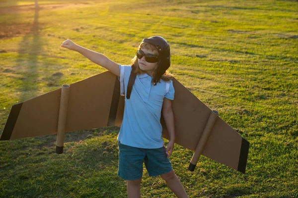 En ung resenär med ryggsäcksvingar. Barnlek pilot flygare och drömmar utomhus i parken. Drömmer, frihet och resande koncept. — Stockfoto