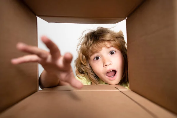 Ragazzo disimballaggio e apertura scatola di cartone, e guardando dentro con faccia a sorpresa. Bambino ragazzo guardando sorpreso in un regalo. — Foto Stock